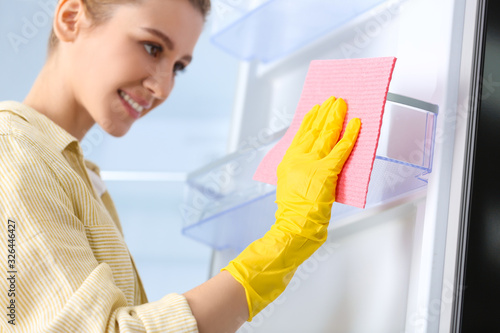 Woman in rubber gloves cleaning empty refrigerator at home, focus on hand with rag