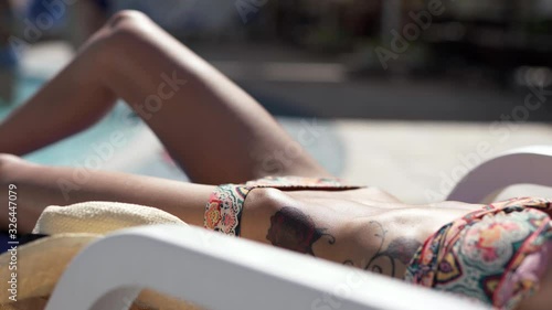 beautiful shapely Caucasian bikini woman with fit body and flat belly lying at pool edge on desk chair and sunbathing. woman relaxing at poolside and enjoying sunny summer day photo