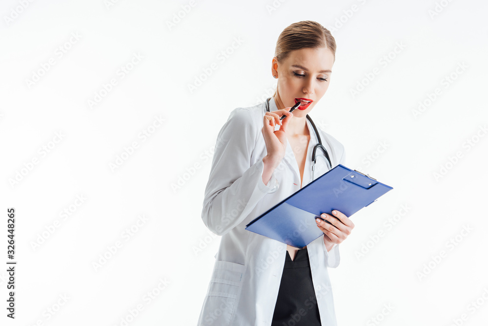 pensive and sexy nurse in white coat looking at prescription while holding clipboard and pen near red lips isolated on white pensive and sexy nurse in white coat looking at prescription while holding clipboard and pen near red lips isolated on white