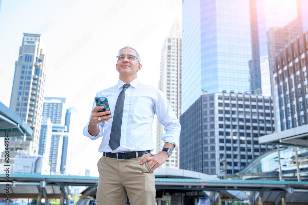 Successful businessman standing outdoors smiling and holding phone in his hands in the background. Successful businessman standing outdoors smiling and holding phone in his hands in the background.