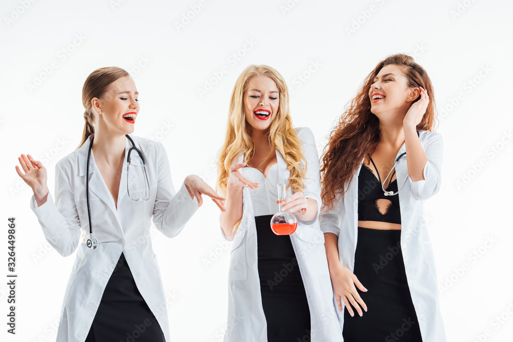 sexy nurses laughing while looking at glass flask with red liquid isolated on white sexy nurses laughing while looking at glass flask with red liquid isolated on white