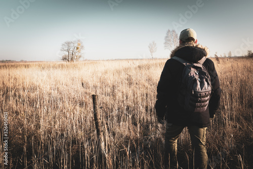 Male traveler with a backpack walking towards the horizon on a wild meadow, Nowiny, Poland © darekb22