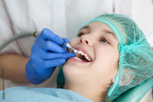 A woman dentist doctor brushes the teeth of a teenage child with a special medical brush. Inspection of the oral cavity of the girl. Modern technologies in dentistry. photo