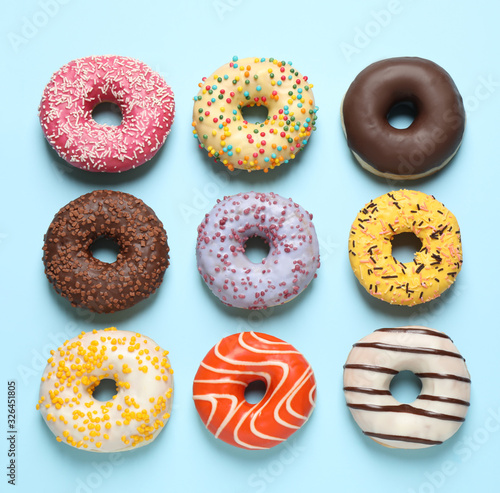 Delicious glazed donuts on light blue background, flat lay