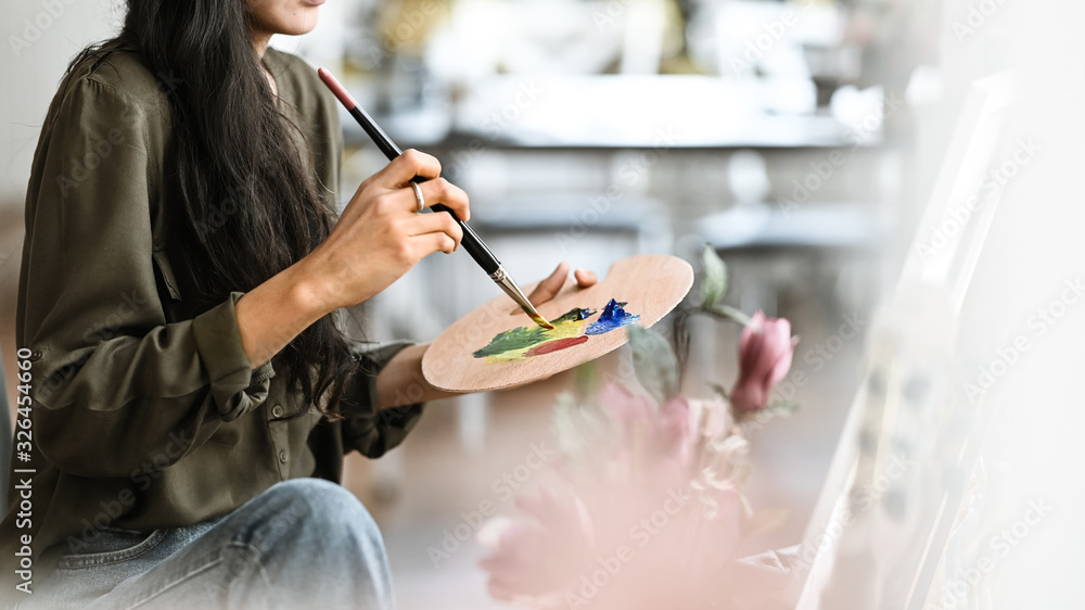 Cropped image of young beautiful artist girl sitting in front the drawing canvas while painting an oil color at the modern studio. Beautiful artist and gallery studio concept. - obrazy, fototapety, plakaty 