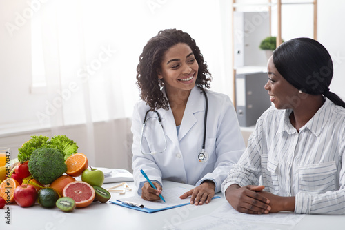 Friendly afro lady nutritionist making patient anamnesis at clinic