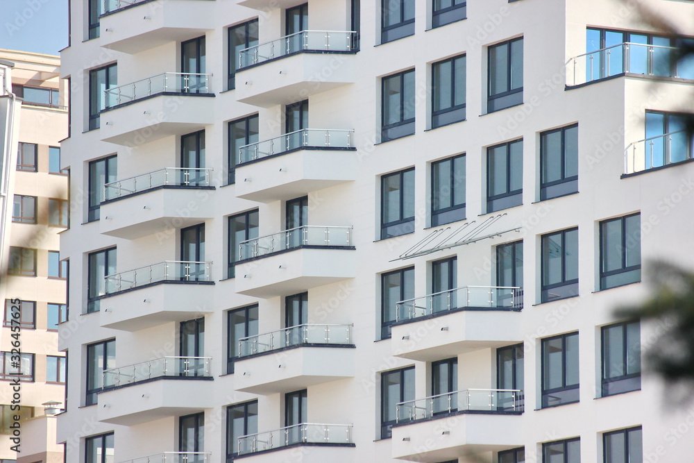 Parts of the modern facade of apartment buildings are made of glass and concrete in beige tones. Plants in the foreground, a combination of nature and houses. Trends in construction