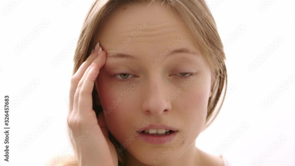 Portrait of a young woman having headache touching her temples and feeling stressed. Close up slow motion shot isolated on white background Portrait of a young woman having headache touching her temples and feeling stressed. Close up slow motion shot isolated on white background