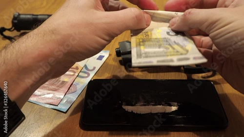 Rolling a bill to snort cocaine. Table full of drugs and weapons.