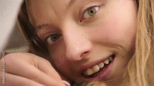 Beautiful young woman lying in bed and playfully peeking through the white sheets. Teasing face expression. Morning fun and happy relationship concept