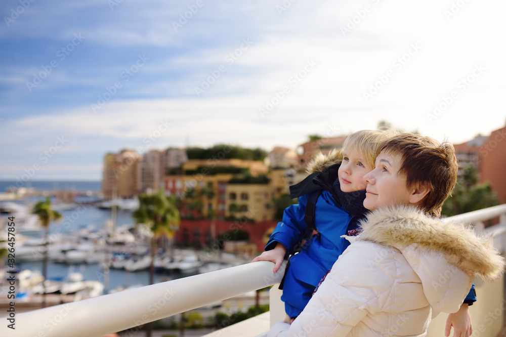 Grandmother and her little grandchild looking on yachts and boats in port of Monaco in winter day.