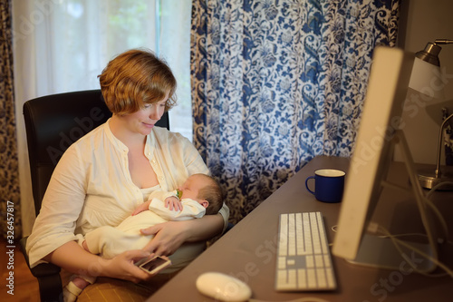 Young mother holding baby, chating by smartphone and working pc at home. Motherhood, business, housework.