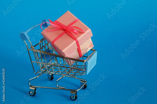 Подарок Gift in the shopping cart on a blue background. Selective focus.