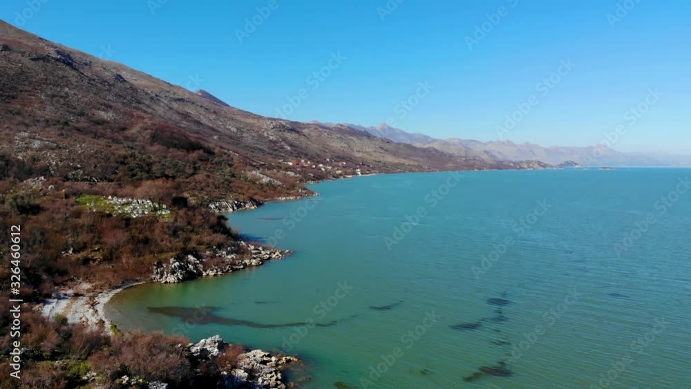 Mountain slope with dry trees and bushes and cliffs on shore of beautiful lake with turquoise water under clear blue sky Mountain slope with dry trees and bushes and cliffs on shore of beautiful lake with turquoise water under clear blue sky