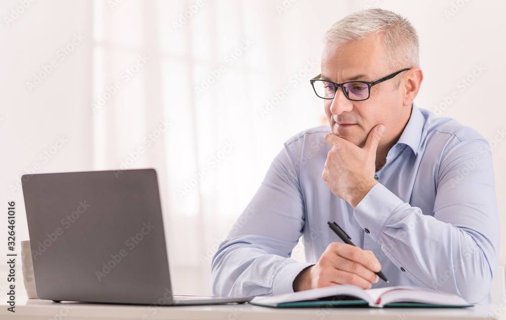 Senior man using laptop at home and writing Senior man using laptop at home and writing