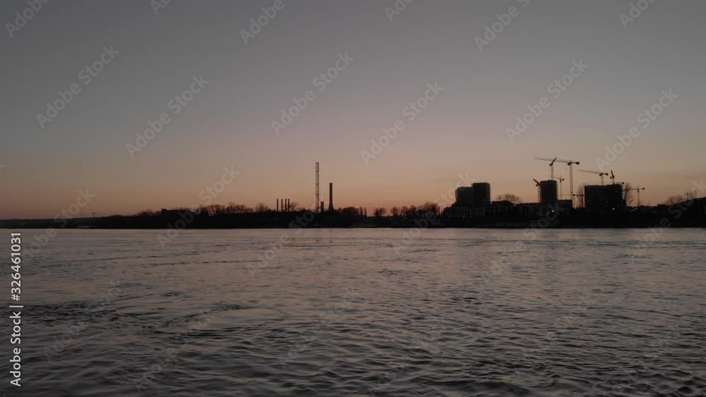Static wide low angle view of a power plant under construction at sunset on a river bank. Industrial buildings with cranes. Static wide low angle view of a power plant under construction at sunset on a river bank. Industrial buildings with cranes.