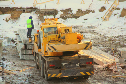 Yellow truck-mounted truck mounted crane at a construction site in winter amid snow in Russia