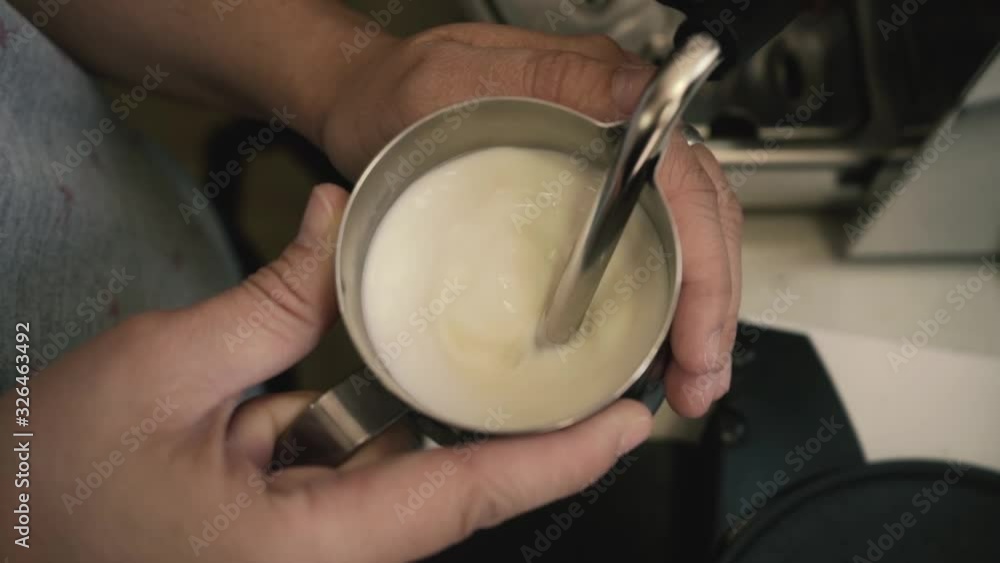 Barista holding a jug of foam texturing milk with the machine vaporizer, view from the top Barista holding a jug of foam texturing milk with the machine vaporizer, view from the top