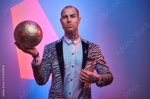 Plakat Fit, handsome, tattooed, bald male model posing in a studio for the photoshoot wearing fashionable custom made zebra striped style tuxedo and rose patterned shirt, looking on a camera, holding a