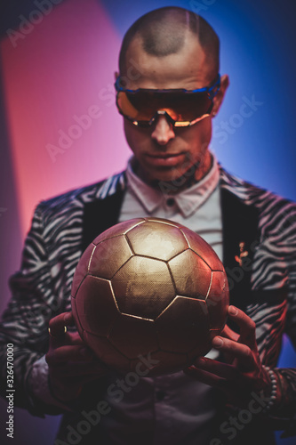 Plakat Fashionable, handsome, tattooed, bald male model posing in a studio for the photoshoot wearing fashionable custom made zebra striped style tuxedo, glasses and rose patterned shirt, looking on a golden