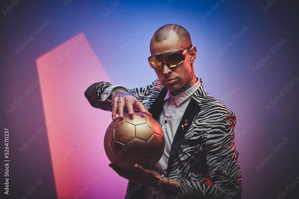 Fashionable, handsome, tattooed, bald male model posing in a studio for the photoshoot wearing fashionable custom made zebra striped style tuxedo, glasses and rose patterned shirt, looking on a golden <span>plik: #326470237 | autor: Fxquadro</span>