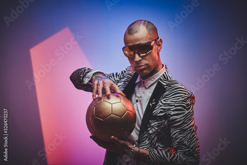 Plakat Fashionable, handsome, tattooed, bald male model posing in a studio for the photoshoot wearing fashionable custom made zebra striped style tuxedo, glasses and rose patterned shirt, looking on a golden