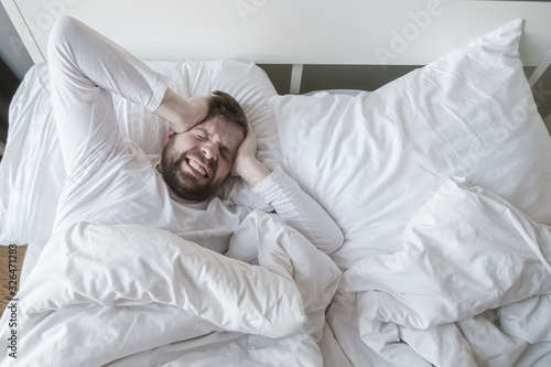 Man in bed suffers from a headache or a hangover  he clenches head in his hands and grins his teeth from pain.