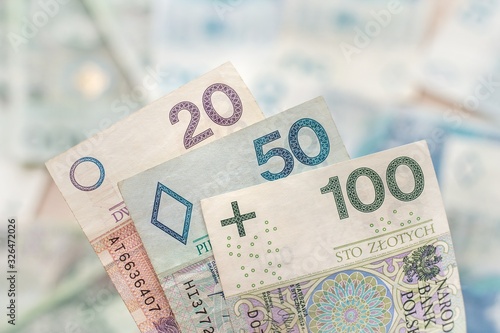 Banknoty o nominałach 20, 50 i 100 zł leżą na pierwszym planie. W tle banknoty o różnych nominałach.
