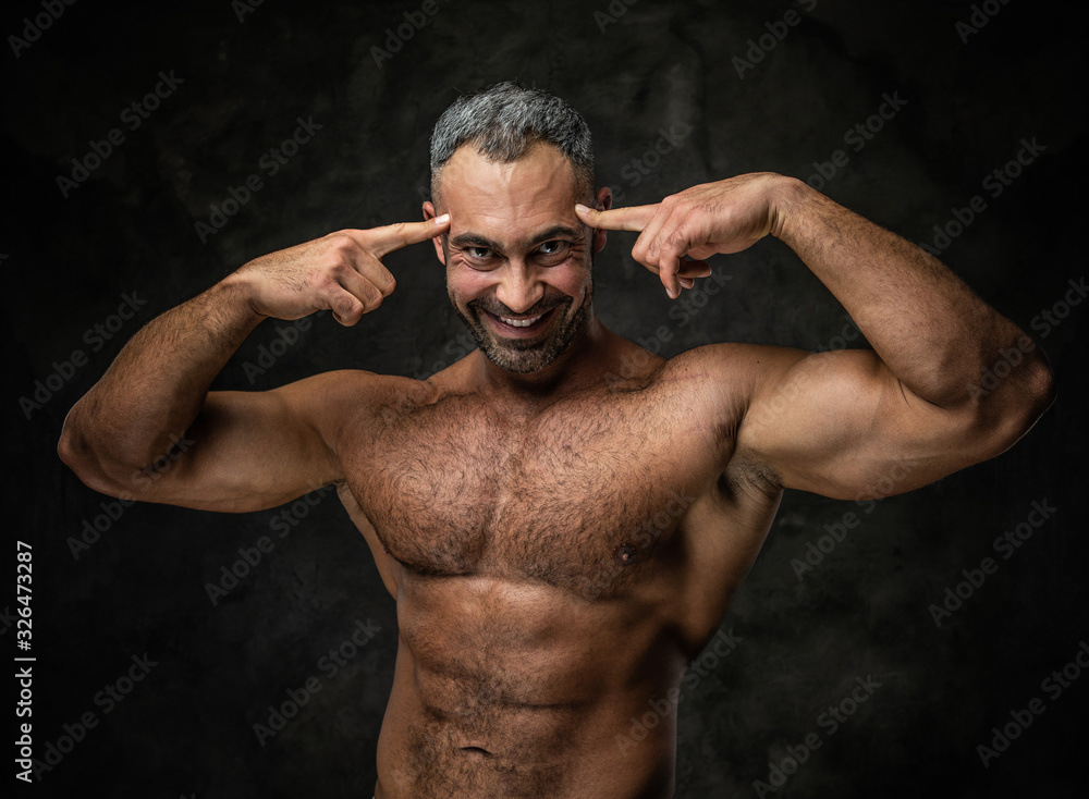 Handsome, adult, fit muscular caucasian man coach posing for a photoshoot in a dark studio under the spotlight, showing a thinking gesture with his hands and smiling