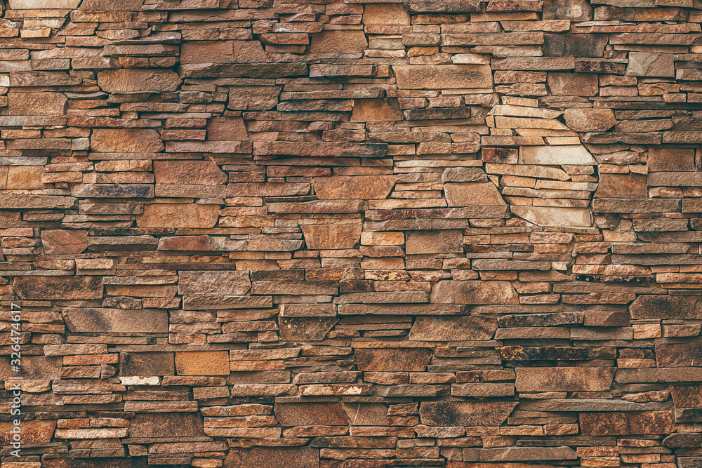 Fototapeta premium Abstract pattern of brown stone texture. Brick wall background. Rough granite surface. Cracked rock. Decorative tile on facade of building.