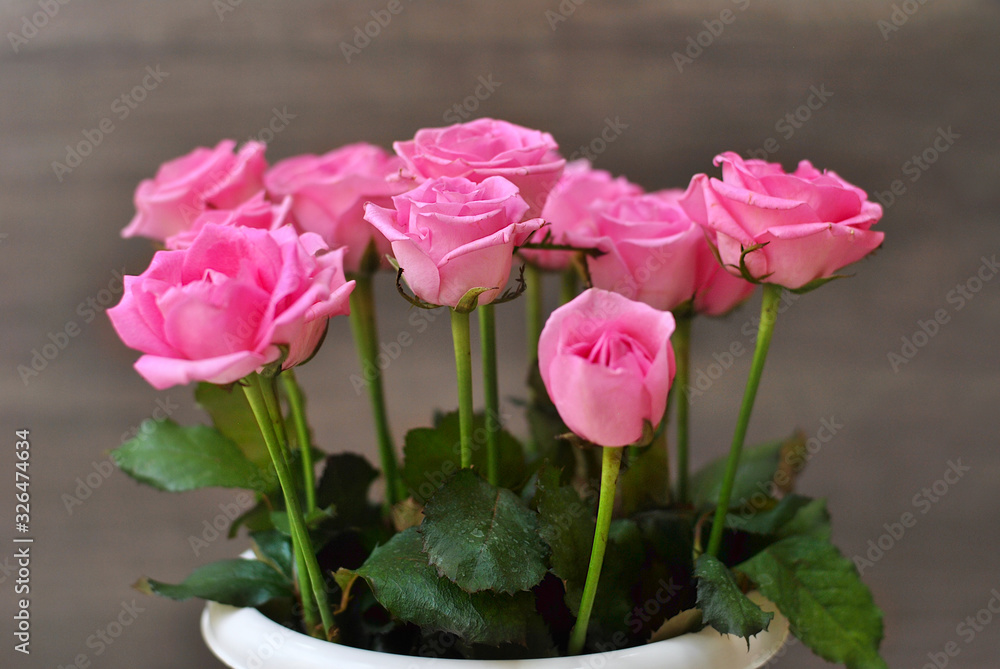 Beautiful lush bouquet of pink roses flowers on the wooden background. Stylish floristic composition in the long vertical vase. Spring time and holidays concept, interiors decorating Beautiful lush bouquet of pink roses flowers on the wooden background. Stylish floristic composition in the long vertical vase. Spring time and holidays concept, interiors decorating