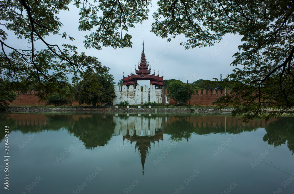 Mandalay Palace wall and moat under grey sky, Myanmar. Photo with foliage frame