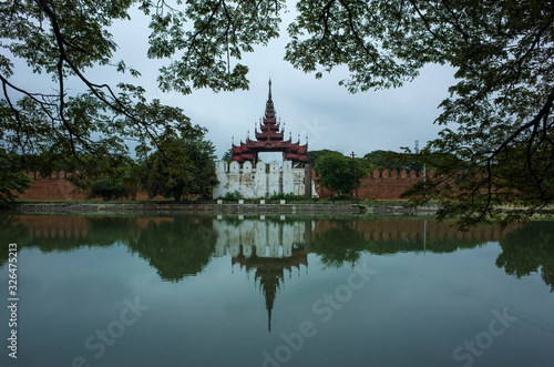 Mandalay Palace wall and moat under grey sky, Myanmar. Photo with foliage frame