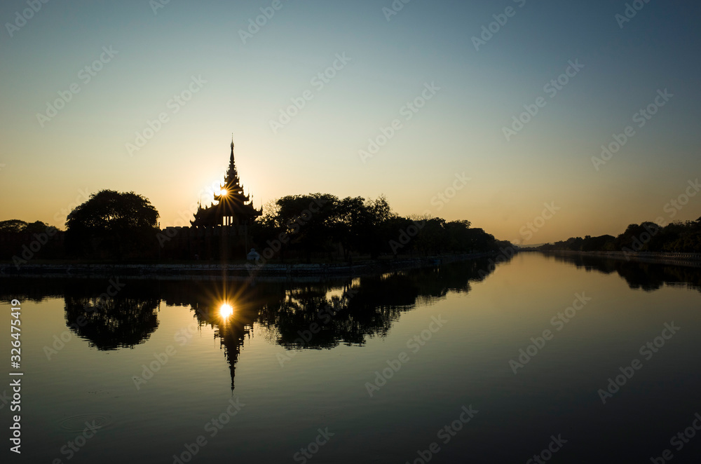 Mandalay Palace wall and moat picturesque silhouette with twilight sky in sunset with sun reflection in water, Myanmar