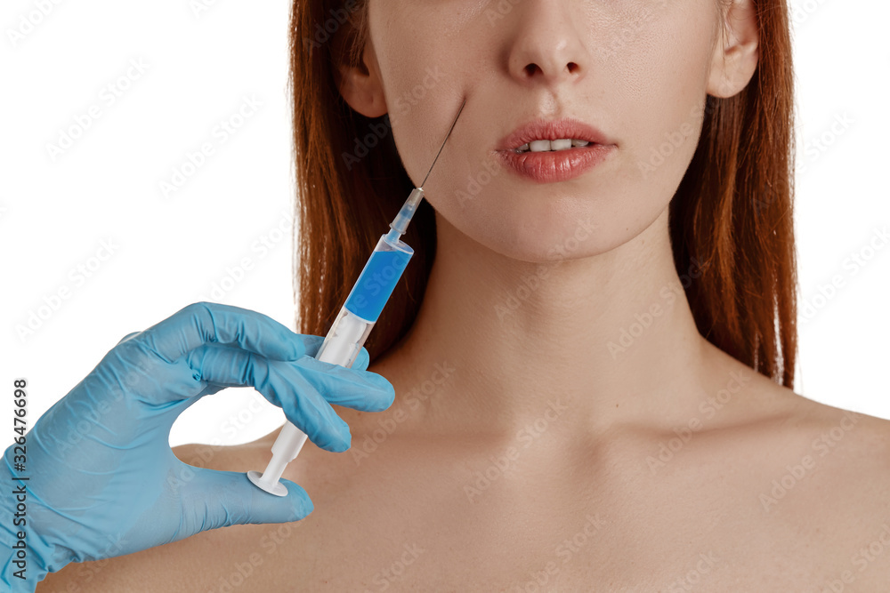 A young girl receives a cosmetic injection using Botox or hyaluronic acid, an injection of HA collagen. Doctors hands make an injection in the face. Cosmetic procedures. A young girl receives a cosmetic injection using Botox or hyaluronic acid, an injection of HA collagen. Doctors hands make an injection in the face. Cosmetic procedures.