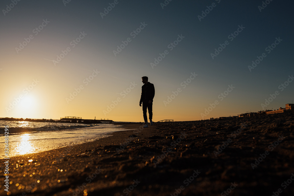 Young, sexy man is walking at the beach into a beautiful sunset. Wonderful landscape. Lido di Ostia, Rome, Italy.