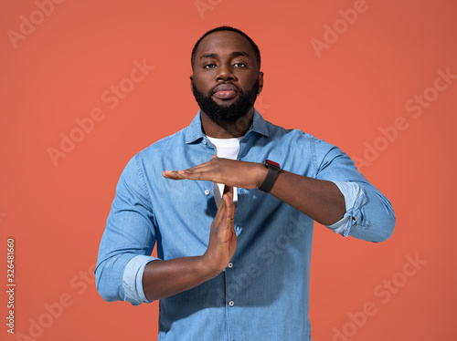 I need break. Man making a timeout gesture. Photo of african man in casual outfit on coral background.