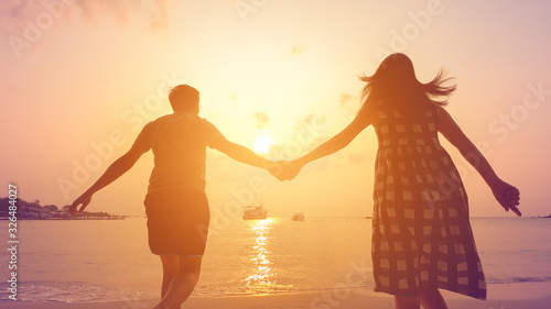 фотографія Happy couple holding each other hands walking to the sea at sunset
