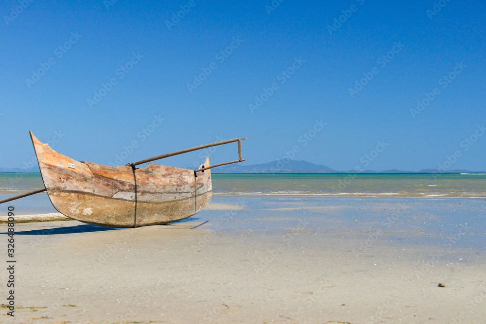 canoe on the sand of the beach at low tide under the blue sky with the sea and its waves coming from the mountain on the horizon canoe on the sand of the beach at low tide under the blue sky with the sea and its waves coming from the mountain on the horizon