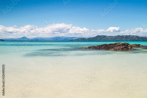 rock on the beach of a turquoise blue sea with mountains on the horizon