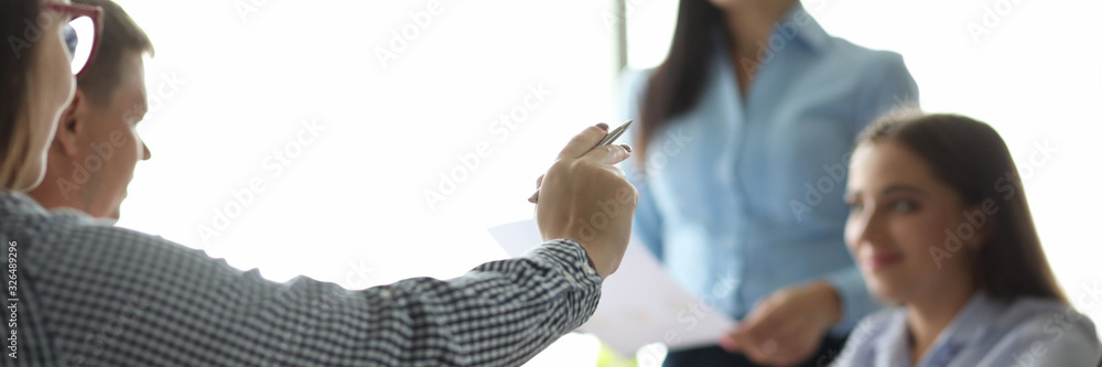 Focus on male hand holding pen. Man pointing at something with ballpen. Colleagues sitting at table in office and discussing annual report. Teamwork concept Focus on male hand holding pen. Man pointing at something with ballpen. Colleagues sitting at table in office and discussing annual report. Teamwork concept