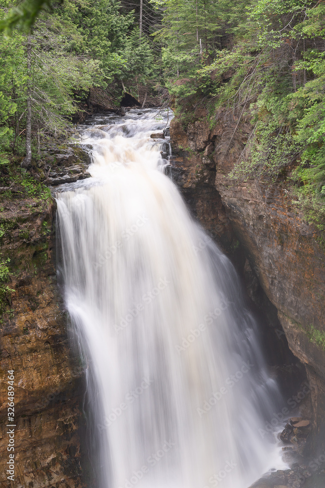 Naklejka premium Jedwabiście gładka woda górników spada w Pictured Rocks National Lakeshore, pędząc przez skały i zanurzając się w kanionie poniżej