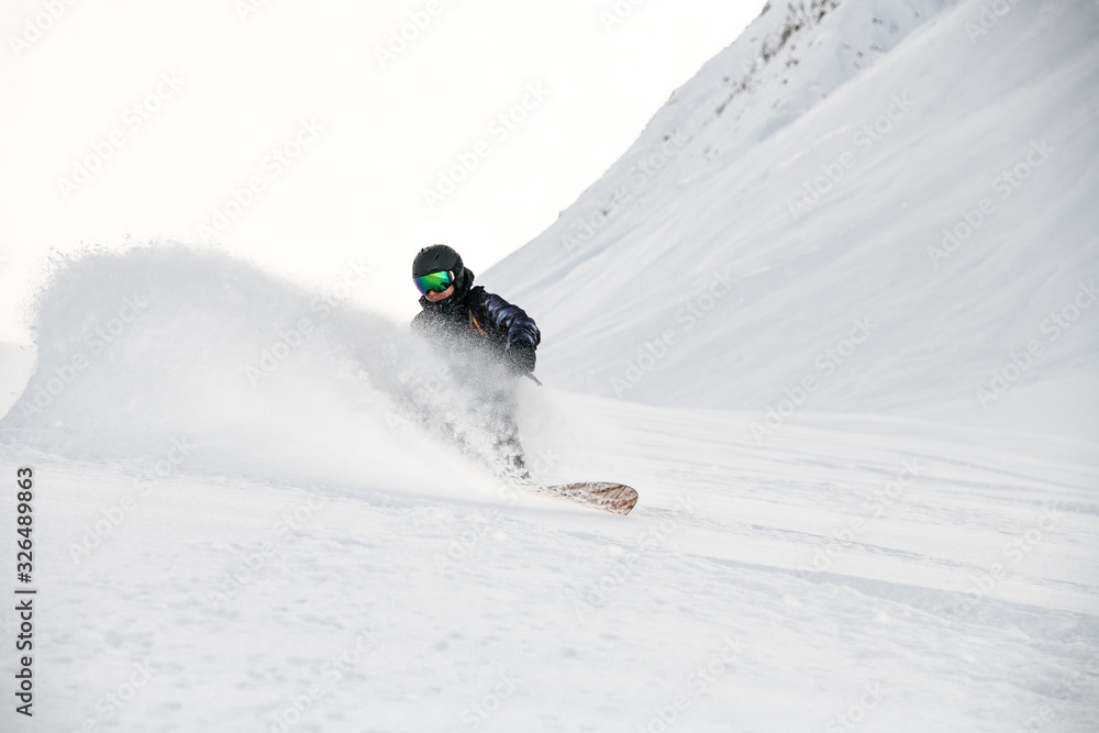 Freerider in full equipment rides on a snowboard in mountains