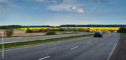 Road and yellow blooming rape fields on background. Picturesque spring scenery.