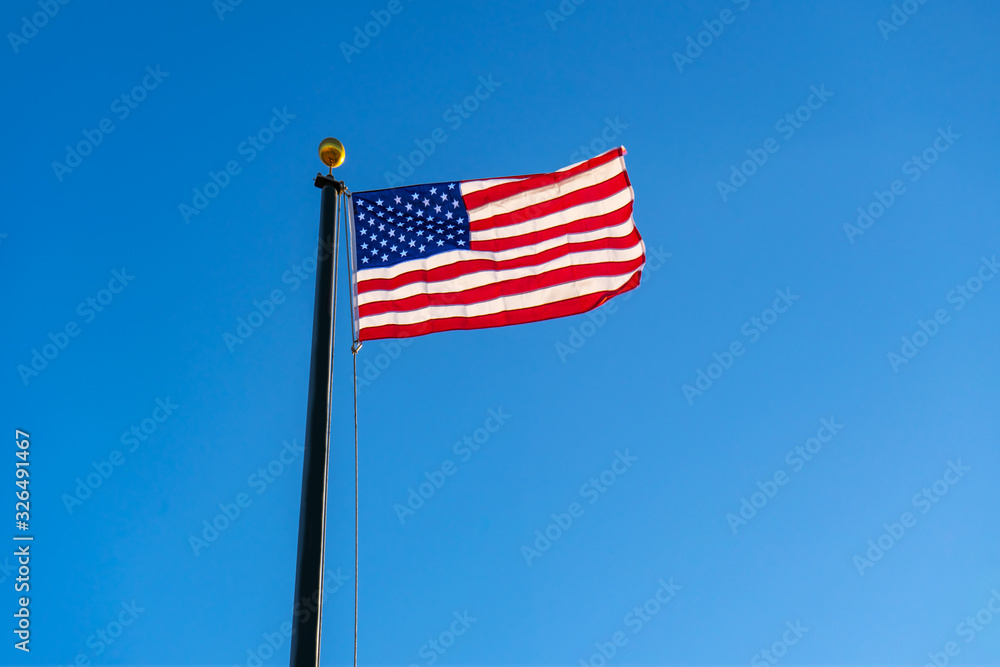 United States of American flag waving in the wind on clear blue sky in background United States of American flag waving in the wind on clear blue sky in background