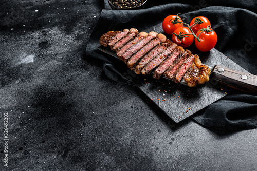 Grilled sliced strip loin steak on a meat cleaver. Black background. Top view. Copy space