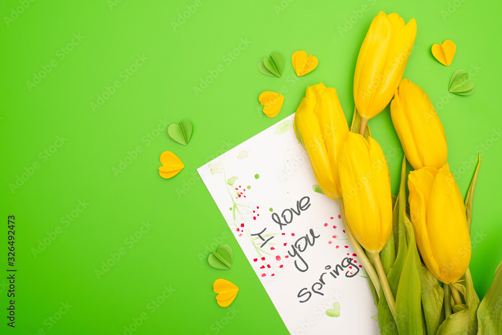 Top view of yellow tulips, card with I love you spring lettering and decorative hearts on green background