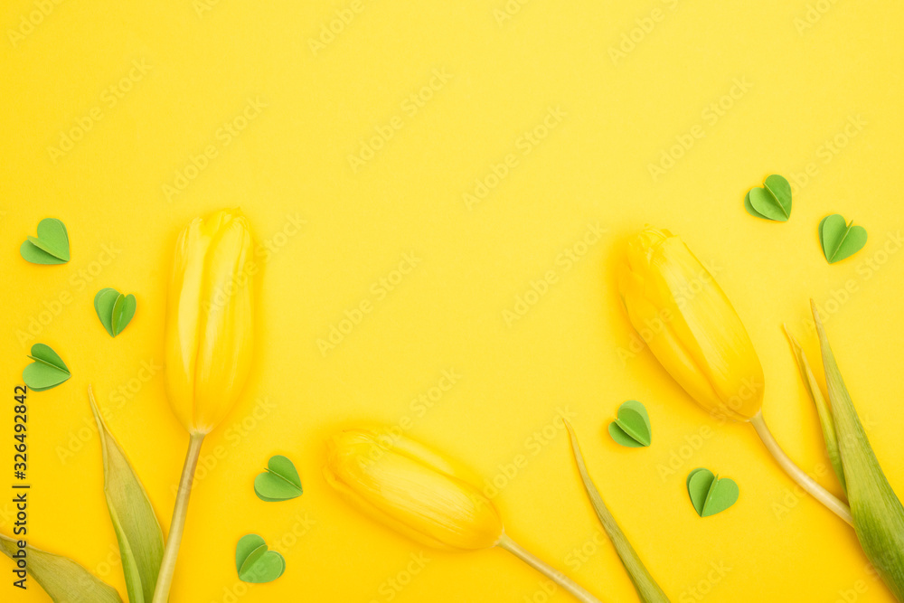 Top view of tulips and decorative green hearts on yellow background, spring concept