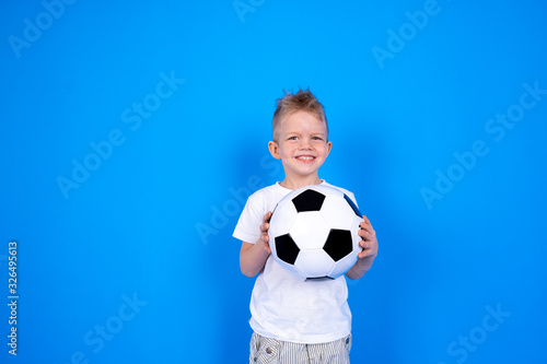 Soccer fans. Smiling caucasian child boy holding soccer ball in hands over blue studio background. Copyspace. Football game © Наталия Кузина