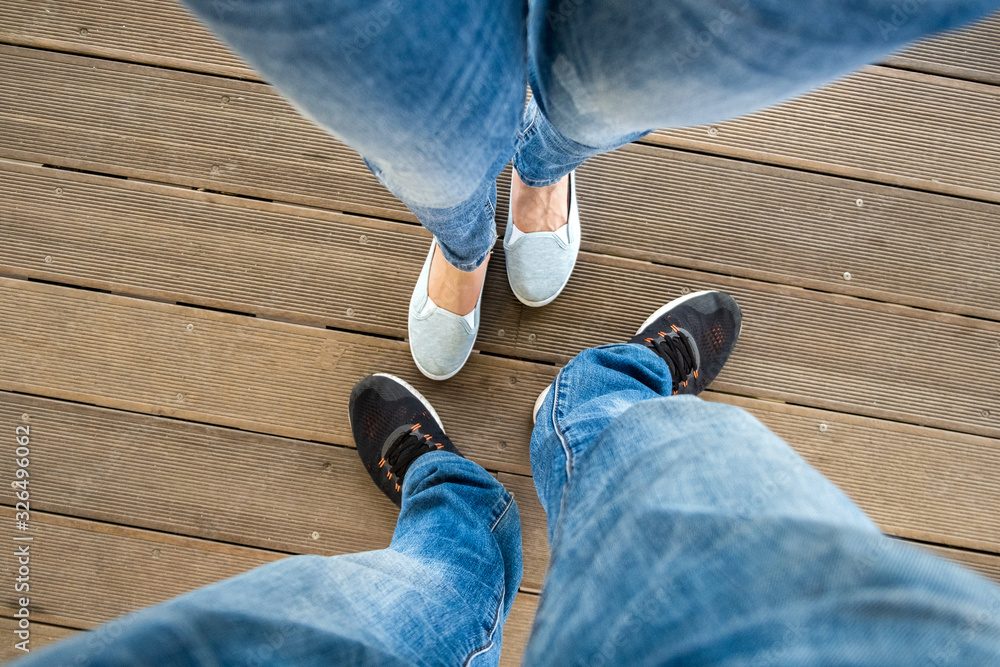 Top down view of legs in denim jeans pants and light summer sneakers standing on wooden floow.